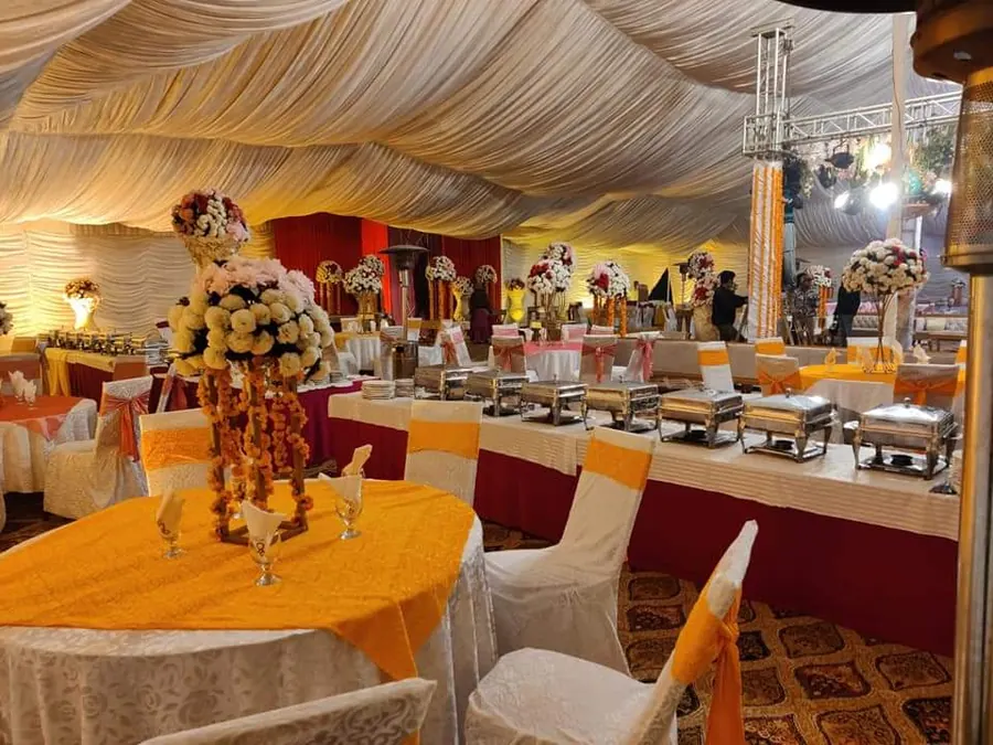 A buffet line of chafing dishes with marigold arrangements under a marquee