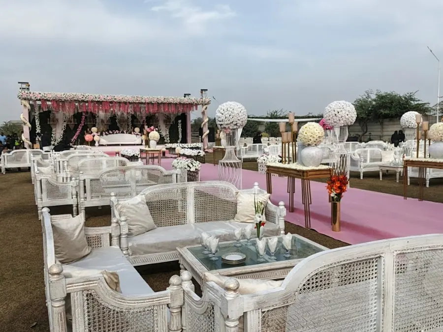 White rattan sofas with cushions and a pink carpet aisle at an outdoor event