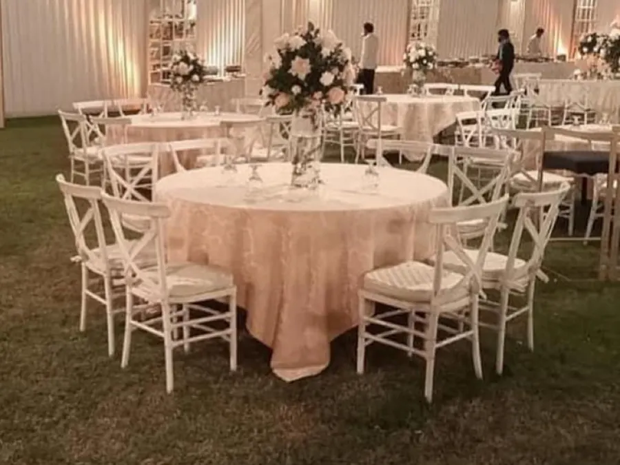 Round tables with white flowers and chairs set out on a lawn for an evening event